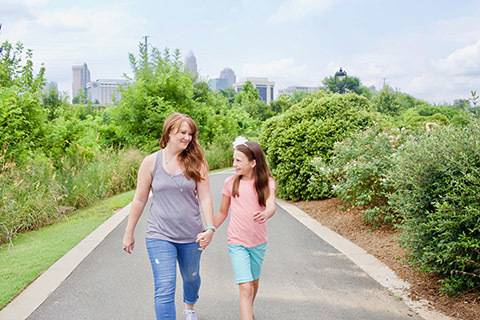 mother and daughter walking along city greenway smiling