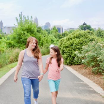 Women and young girl walking on city greenway holding hands